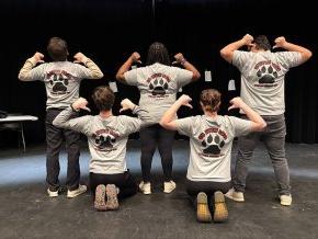 The five members of Bear With Us show the backs of their t-shirts on the stage